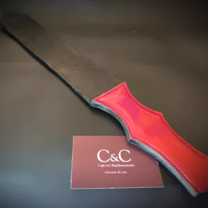 Close-up of a red leather strap with teal edge on a dark surface, a burgundy card with 'C&C' partially visible nearby.