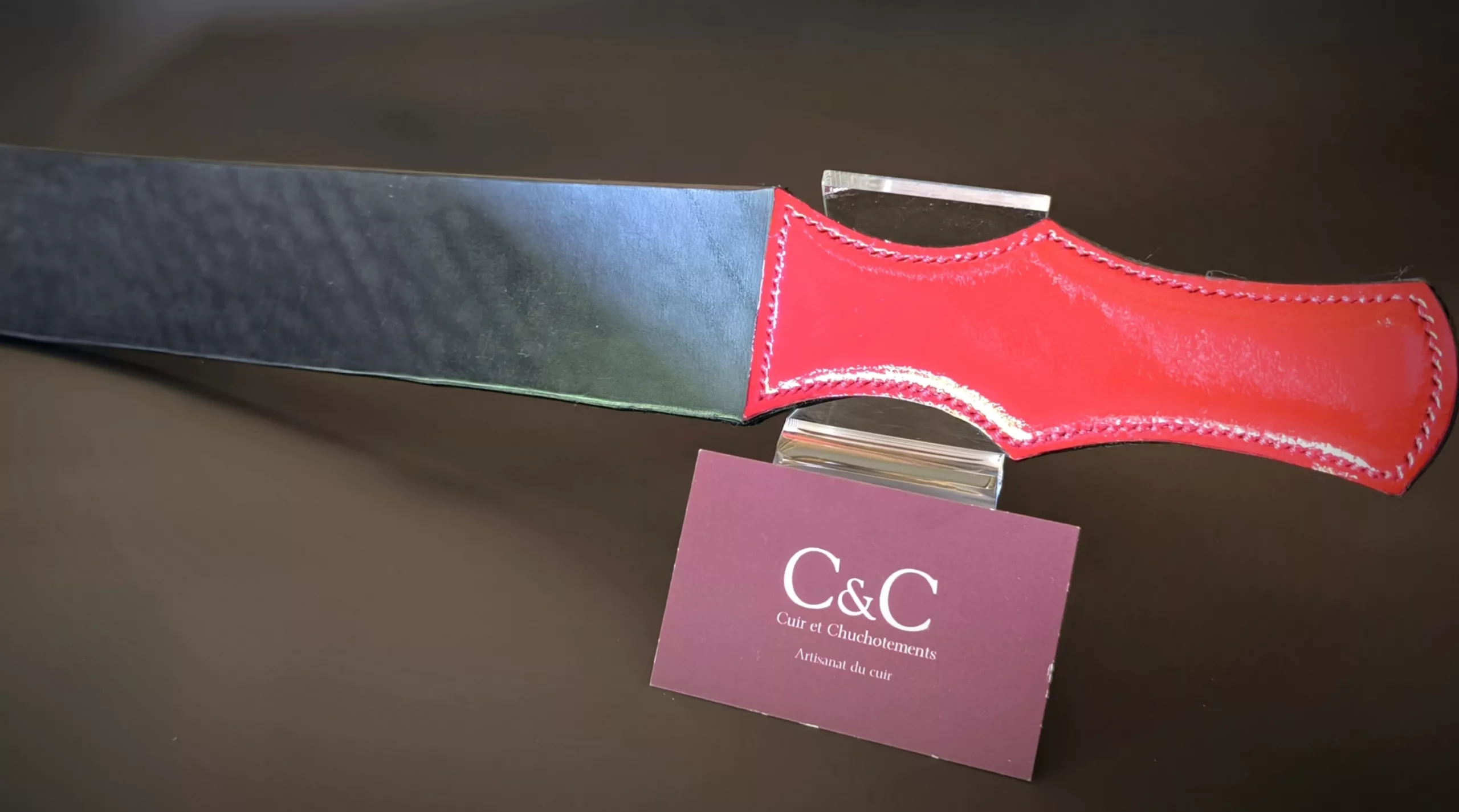 Red leather sheath stitched around a blade, showing a black blade and brand card reading C&C nearby.